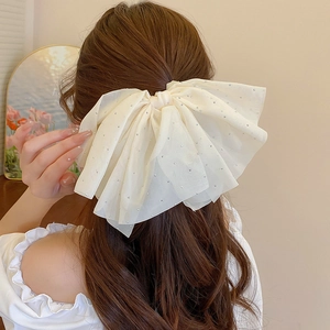 Close-up of a cream mesh bow hair clip with pearls and long tassels on a model
