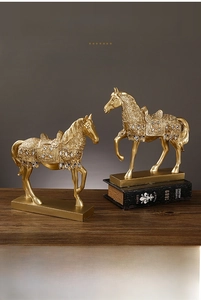 Close-up of golden horse statues with ornate crystals on a luxury wooden desk