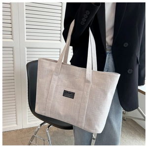 Close-up of a large beige canvas tote bag with a woven texture and outer pocket