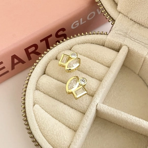 Close-up of geometric 18K gold plated earrings with clear stones in a beige jewelry box