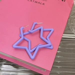 Close-up of purple matte star earrings resting on a bright pink fashion book cover