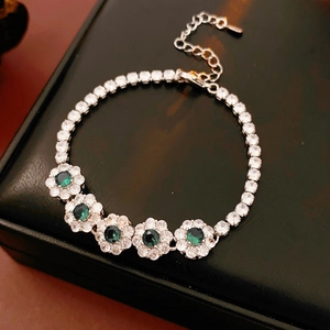 Détail macro du bracelet fleurs argentées avec zircons verts sur fond en cuir noir
