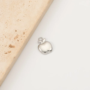 Detailed macro view of silver apple-shaped pendant on a textured beige stone background