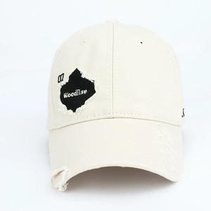 Close-up of distressed beige cotton baseball cap with vintage patch embroidery and ripped detail