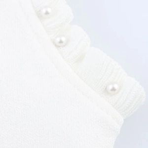 Macro shot of delicate white knit dress edge featuring ruffled trim and pearl accents