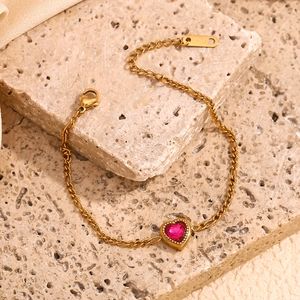 Detailed close-up of 18K gold Figaro chain bracelet featuring a red heart zircon stone