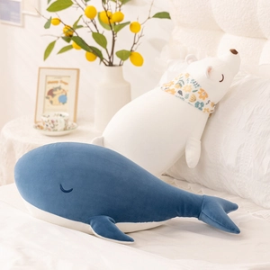 Plush polar bear with scarf and blue whale soft toys resting on a cozy white bed