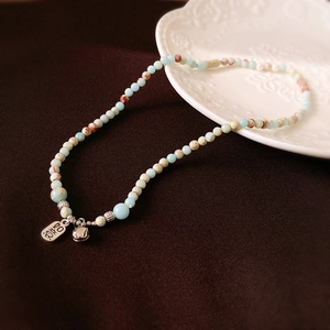 Detailed macro of a beaded necklace with Ruyi pendant and bell on a ceramic plate