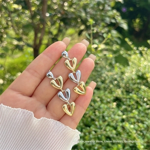 Détail de boucles d'oreilles pendantes à trois cœurs imbriqués en or 18 carats et argent