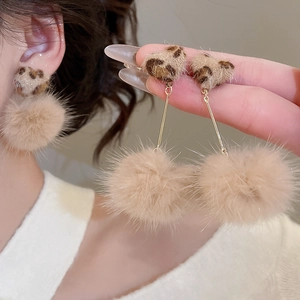 Detail of leopard print heart and beige fur ball pendant earrings on model side view
