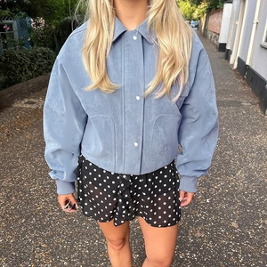 Detail of light blue faux suede jacket featuring snap buttons and ribbed cuffs