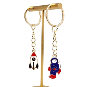 Space-themed astronaut and rocket enamel keychain set on a gold T-stand with white background