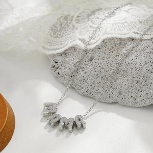 Detailed close-up of a silver MAMA pendant necklace with zircon inlay on a textured stone
