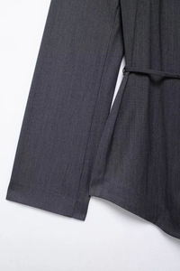 Detail view of dark gray pinstripe blazer with waist belt and textured woven fabric