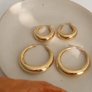 Golden hollow hoop earring set in two sizes on a white ceramic tray with dried leaves