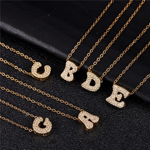 Detail of gold cursive alphabet necklaces with sparkling zircon inlay on black background