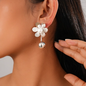 Close-up of floral silver earrings with white pearls and metal spheres on a female model