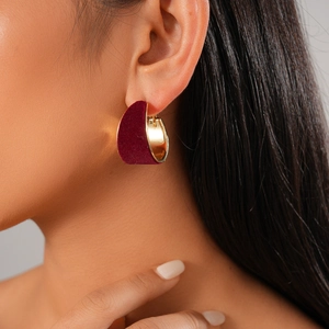 Close-up of a model wearing a dark red velvet geometric hoop earring with gold metal accents