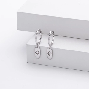 Macro detail of silver starburst engraved oval charm earrings on white display