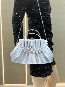 Close-up of pleated silver satin evening bag with rhinestone flowers and metal handle