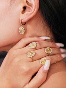 Close-up of gold 18k plated Virgin Mary medallion earrings and rings set with zircon
