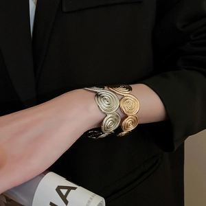 Detail of artistic metallic spiral cuff bracelet with wavy texture on a black suit sleeve