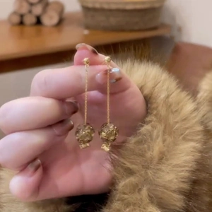 Elegant gold long chain drop earrings with spherical charms held against a warm fur background