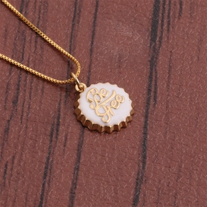 Detailed close-up of a gold 18K plated Be Free bottle cap pendant on a brown surface