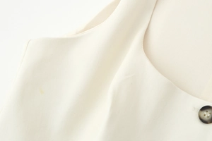 Detail shot of beige V-neck vest showing woven fabric texture and dark textured button