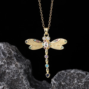 Macro shot of colorful dragonfly pendant with gold chain on dark textured stone
