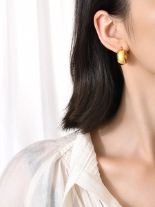 Close-up of elegant 18K gold hollow geometric earrings worn by a model in soft light