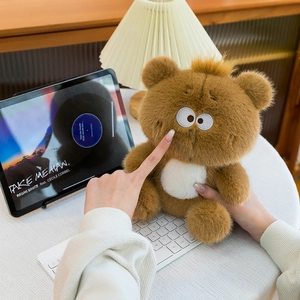 Person holding a brown plush bear with large eyes in a cozy home office setting