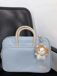 Hellblaue Laptoptasche mit khakifarbenen Griffen und Bärenanhänger auf dem Bürostuhl
