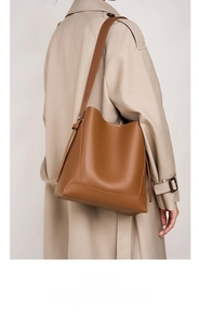 Seitenansicht einer braunen Leder-Beuteltasche getragen mit einem beigen Trenchcoat