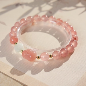 Macro detail of strawberry quartz beaded bracelet with gold spacers and a pink carved charm