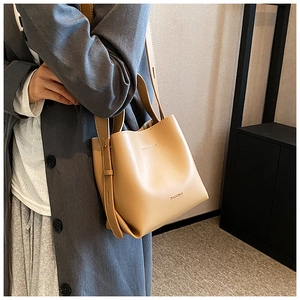 Brown leather bucket bag with long strap worn by a model in a minimalist setting