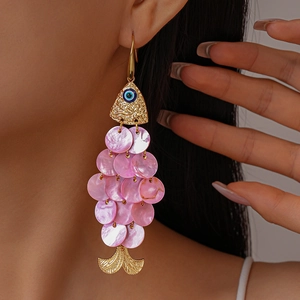 Close-up of a gold fish-shaped earring with blue evil eye and pink shell tassels