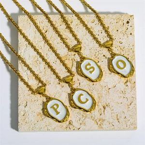 Detail of four gold necklaces with initial S, O, P, C pendants on beige marble