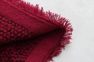 Vista macro detallada del tejido de punto tweed granate con elegante borde de flecos