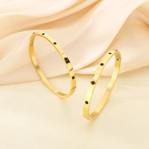 Elegant gold-plated stainless steel bangles with black round accents on beige silk
