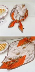 Detailed view of a pleated square scarf with orange floral pattern and wavy edges