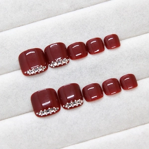 Glossy burgundy press-on toenails with elegant rhinestones arranged in two neat rows