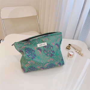 Detail of green jacquard makeup bag with intricate embroidery and simple wish label