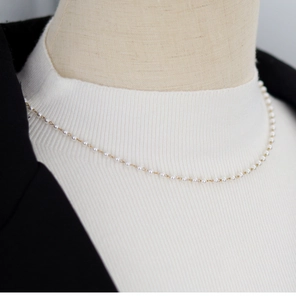 Detail of delicate pearl necklace on gold chain paired with white sweater and black blazer