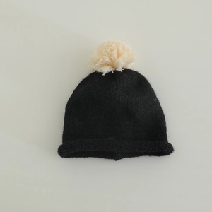 Detailed texture of black knitted beanie featuring a soft off-white fluffy pompom top