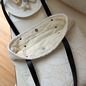 Detailed embroidery texture on a white canvas tote bag with contrast black leather straps