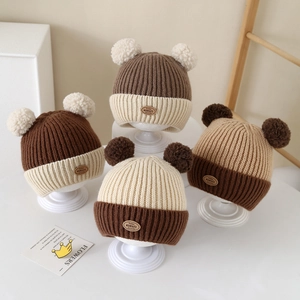 Winter knit baby beanie with two fur pom-poms and leather logo patch in warm color block