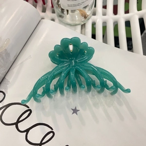 Detail of a large green flower hair claw clip placed on a white magazine background