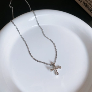 Detailed view of a silver cross bone pendant necklace resting on a white ceramic plate