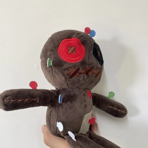 Handcrafted plush voodoo doll with button eyes and colorful needles on white background